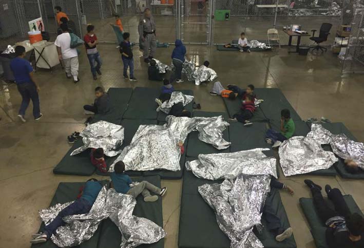 Los niños se encuentran en grandes jaulas de metal dentro de una bodega, rodeados de botellas de agua, bolsas de papitas fritas y grandes láminas de papel aluminio para que se cubran al dormir.