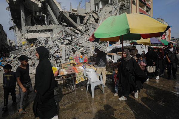Palestinos pasan junto a los quioscos instalados junto a edificios destruidos a lo largo de una calle del campo de refugiados de Al Nusarat, Franja de Gaza.