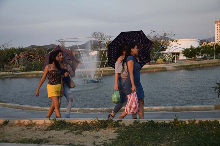 Algunos ciudadanos se protegen de las gotas que brotan de la fuente al pasar por el lugar. Foto: Édgar Fuentes
