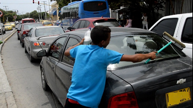 Los menores piden dinero en los semáforos de la ciudad mientras sus padres muestran carteleras con mensajes solicitando ayuda. 