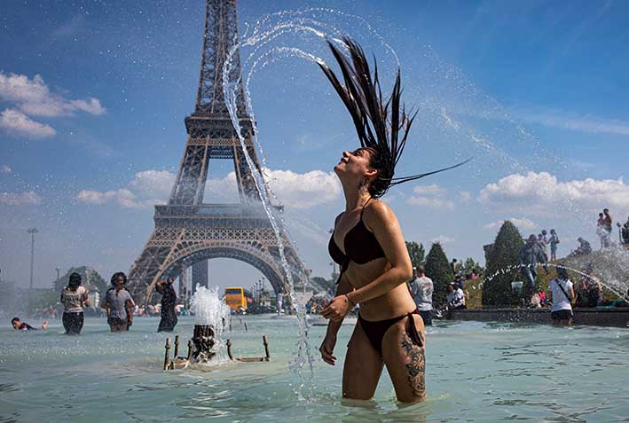 Una turista se refresca con el agua de la fuente de la Plaza del Trocadero, frente a la Torre Eiffel.