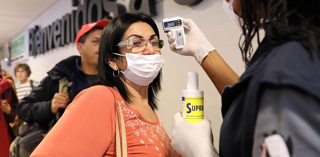 Mujer con tapabocas recibe control de funcionarios, quienes le toman la temperatura en un aeropuerto del país. Foto referencia EFE.