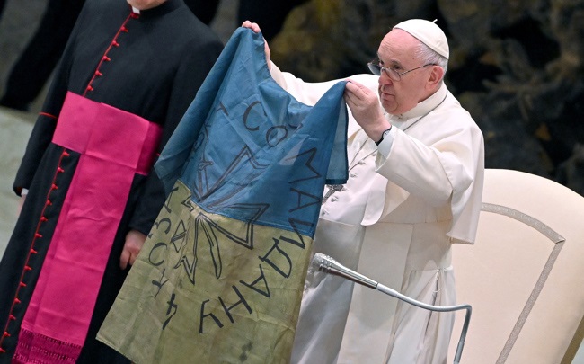 El papa Francisco muestra una bandera de Ucrania que fue enviada desde la localidad de Bucha durante la audiencia semanal en el Salón de Pablo VI en el Vaticano, este miércoles. EFE