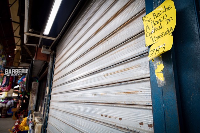 Locales comerciales a medio abrir muestran letreros del precio del dólar y el bolívar digital hoy, en Maracaibo (Venezuela).