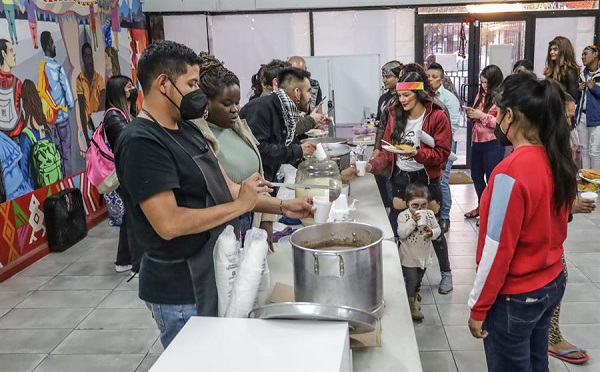 La fotografía muestra a migrantes de diversas nacionalidades se reúnen para recibir alimentación.