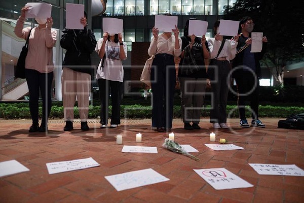 Estudiantes de China continental sostienen hojas de papel en blanco durante una vigilia por las víctimas de la política cero-covid de China.