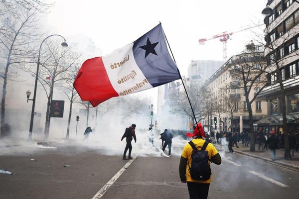 Un manifestante con una bandera francesa camina en medio de los enfrentamientos durante una manifestación contra la reforma de las pensiones del gobierno en París.