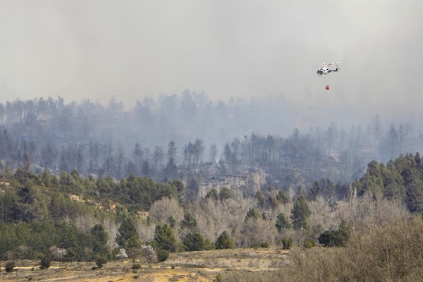 Un helicóptero trata de sofocar un incendio declarado en la localidad castellonense de Villanueva de Viver, visto desde el municipio turolense de San Agustín