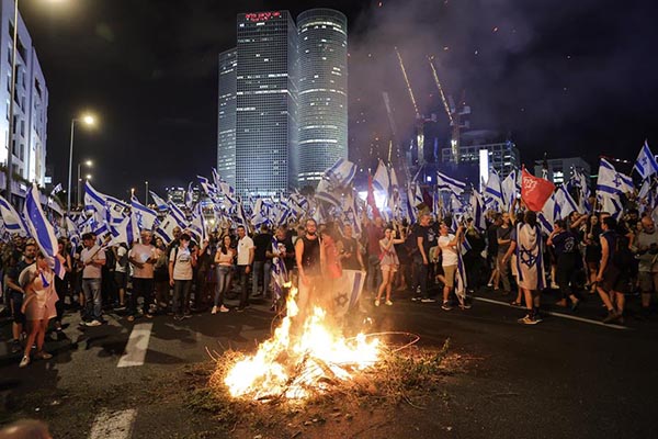 Manifestantes antigubernamentales ondean banderas israelíes y encienden hogueras mientras bloquean la carretera de Ayalon.