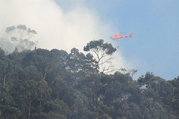 Un helicóptero, que utiliza el sistema Bambi bucket, arroja agua entre el humo que se observa hoy en los cerros orientales en Bogotá 
