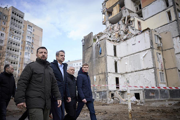 El presidente ucraniano Volodymyr Zelensky y al primer ministro griego Kyriakos Mitsotakis caminando frente a un edificio residencial dañado en un lugar afectado por un ataque con aviones no tripulados rusos.