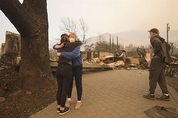Melissa Young recibe un abrazo de un vecino mientras mira los restos de su casa que fue destruida por el incendio forestal. EFE