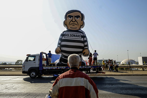 Una persona observa un muñeco alusivo al expresidente de Brasil Jair Bolsonaro durante un desfile, en Brasilia, Brasil). Un grupo de estudiantes brasileños desfiló con un muñeco inflable de Bolsonaro vestido de recluso, un día después de ser condenado a 27 años y tres meses de prisión por golpismo. (Foto EFE/ Antonio Lacerda)