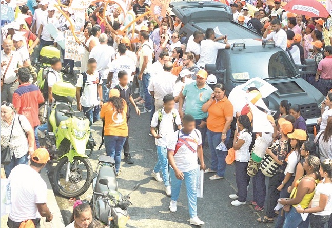 Estudiantes con uniformes de un colegio del Distrito caminan entre los manifestantes frente a la sede de la audiencia que debía adelantarse el día de ayer contra Carlos Caicedo y Rafael Martínez. El primero de ellos llevo lo que parece una pancarta.