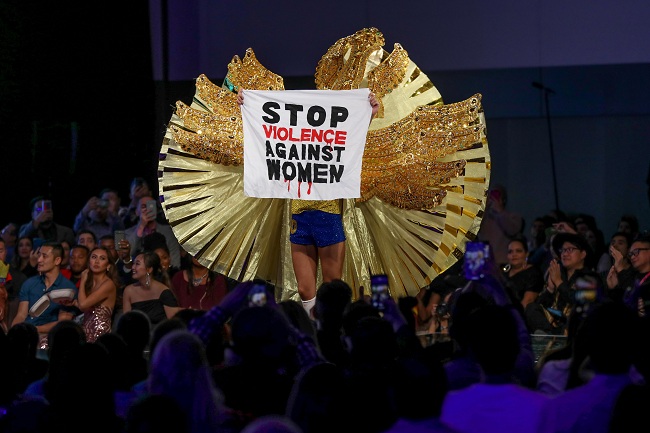 Miss Brasil Julia Horta despliega una pancarta contra la violencia de género durante uno de los desfiles de la ronda preliminar de la gala de Miss Universo celebrada en Atlanta (Georgia) este viernes. EFE/