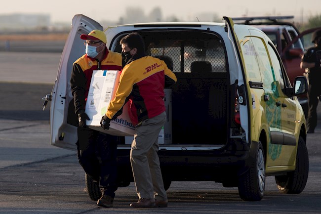 Dos trabajadores de un servicio de mensajería cargan hoy una caja con las primeras 10.000 dosis de la vacuna contra la covid-19 en llegar a territorio chileno, en el grupo de aviación número 10 de la Fuerza Aérea de Chile, en Santiago (Chile). EFE