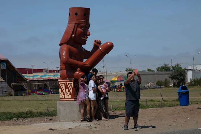 Un grupo de personas posa para una foto frente a una estatua, en Moche (Perú)
