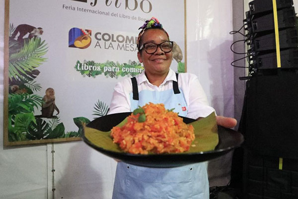 Una de las asistentes del evento mostrando una bandeja que contiene un plato típico de una región específica de Colombia.