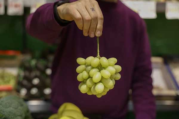 Un frutero muestra un racimo de uvas en un mercado de Madrid. EFE/Juan Carlos Hidalgo